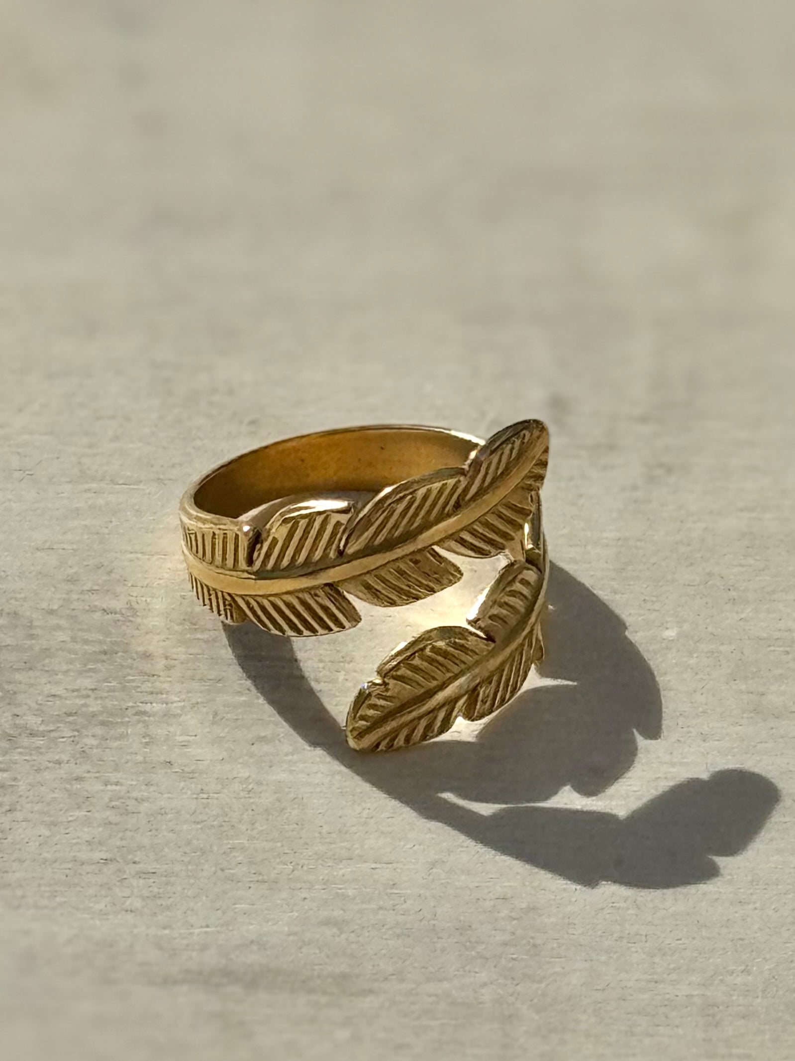 Gold feather-shaped ring on a light gray background