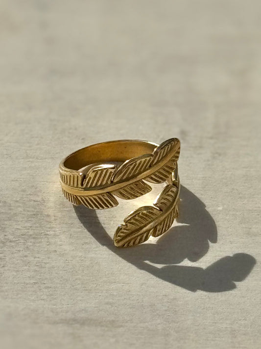 Gold feather-shaped ring on a light gray background