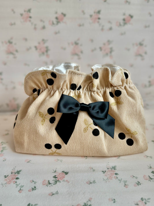 Beige pouch with black polka dots and a bow on a floral background