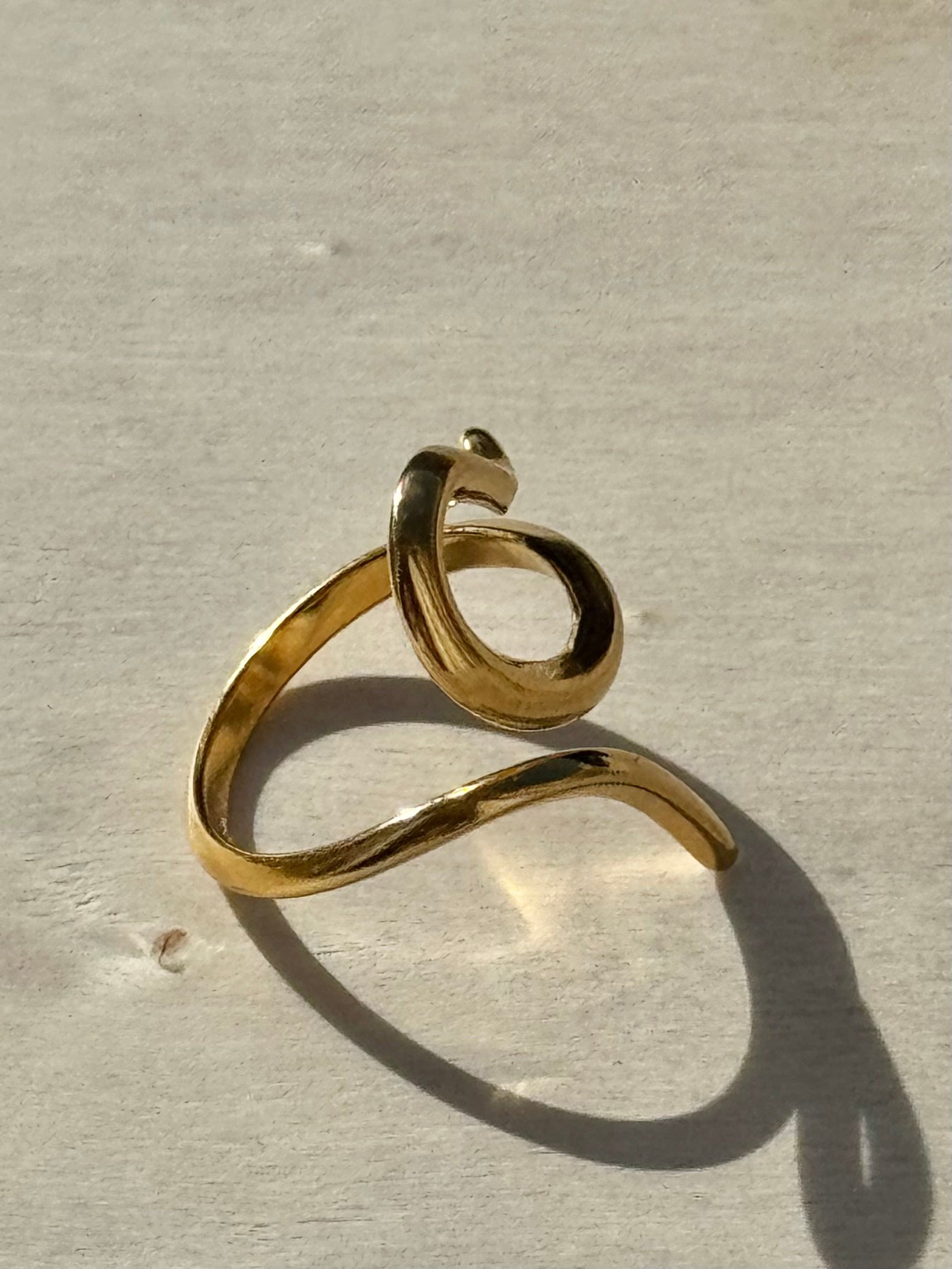 Gold ring with a wavy design on a beige background