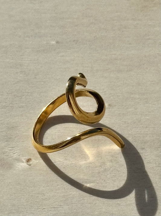 Gold ring with a wavy design on a beige background