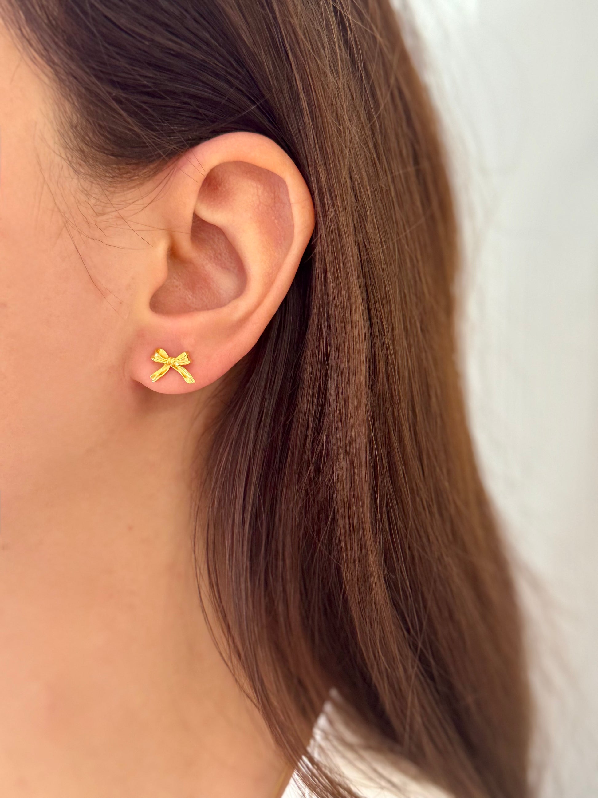 Close-up of an ear wearing a yellow bow-shaped earring with a blurred background