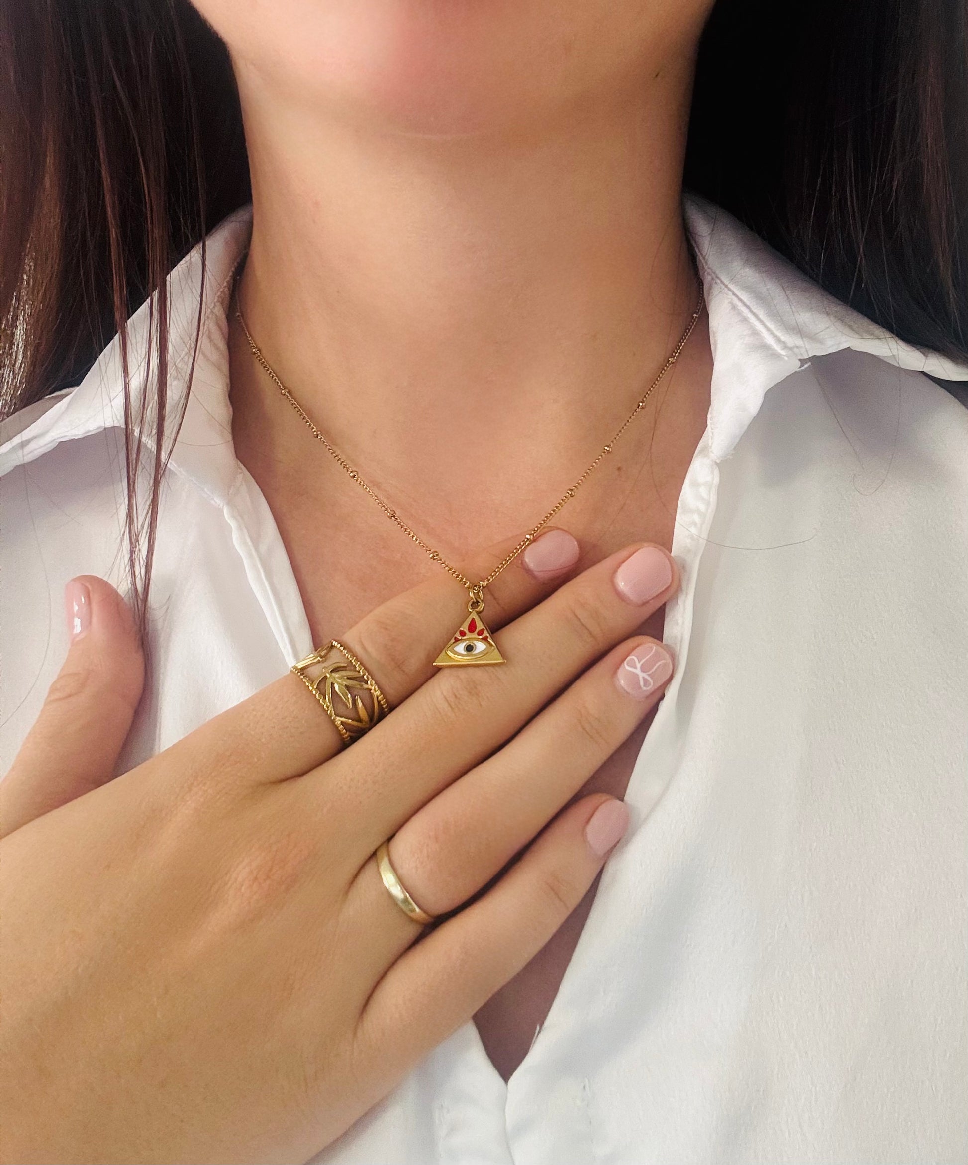 Close-up of gold jewelry including a necklace, ring, and bracelet on a person wearing a white shirt.