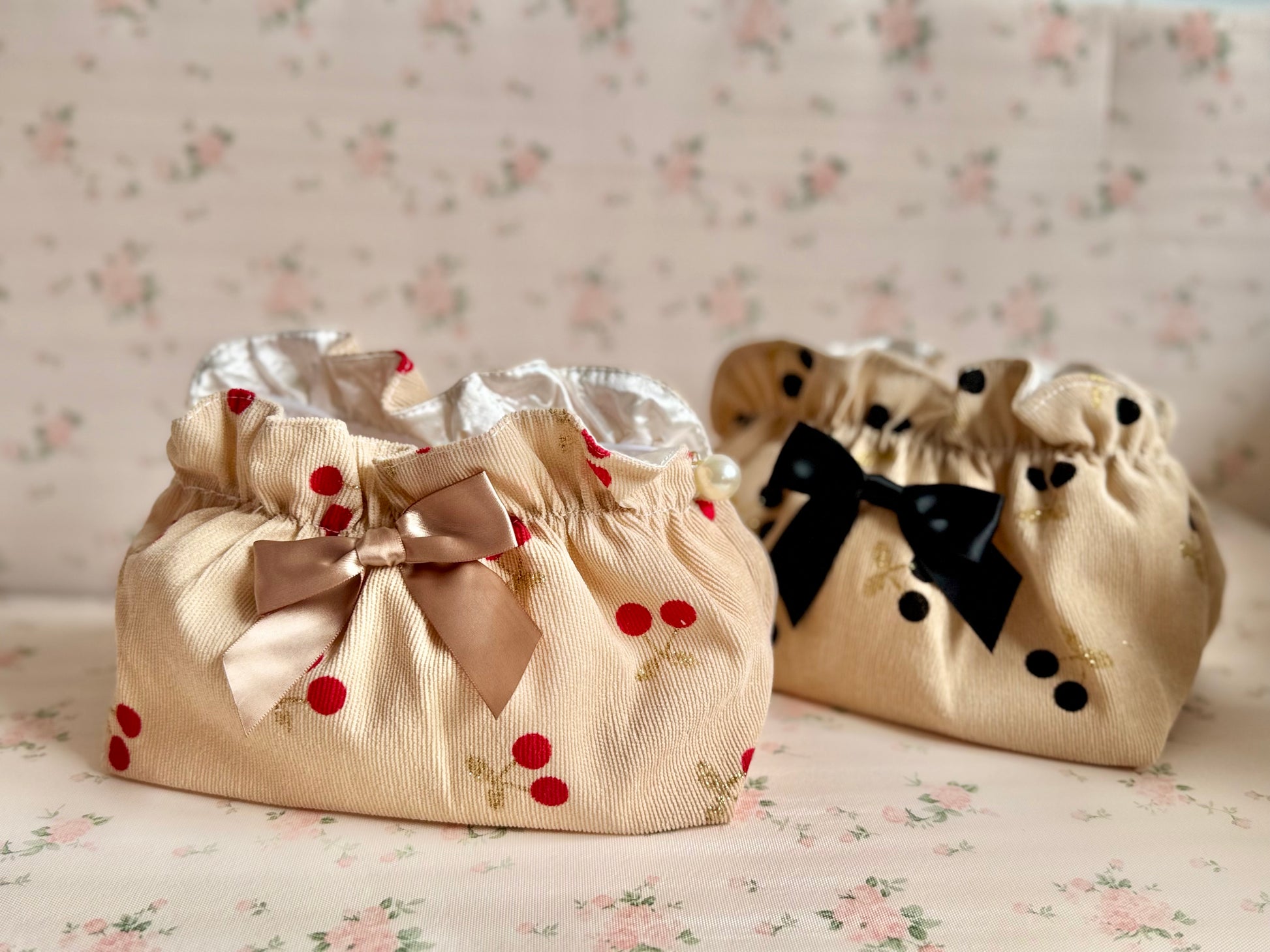 Two decorative bags with ribbons and cherry designs on a floral background