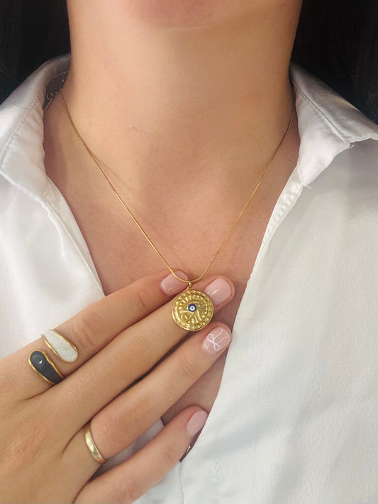 Gold necklace with a pendant held by a hand against a white shirt background