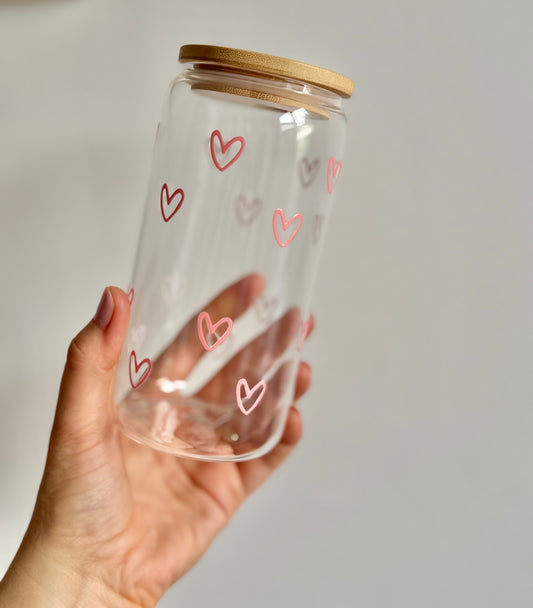 Clear glass jar with pink heart designs and a wooden lid held by a hand against a plain background