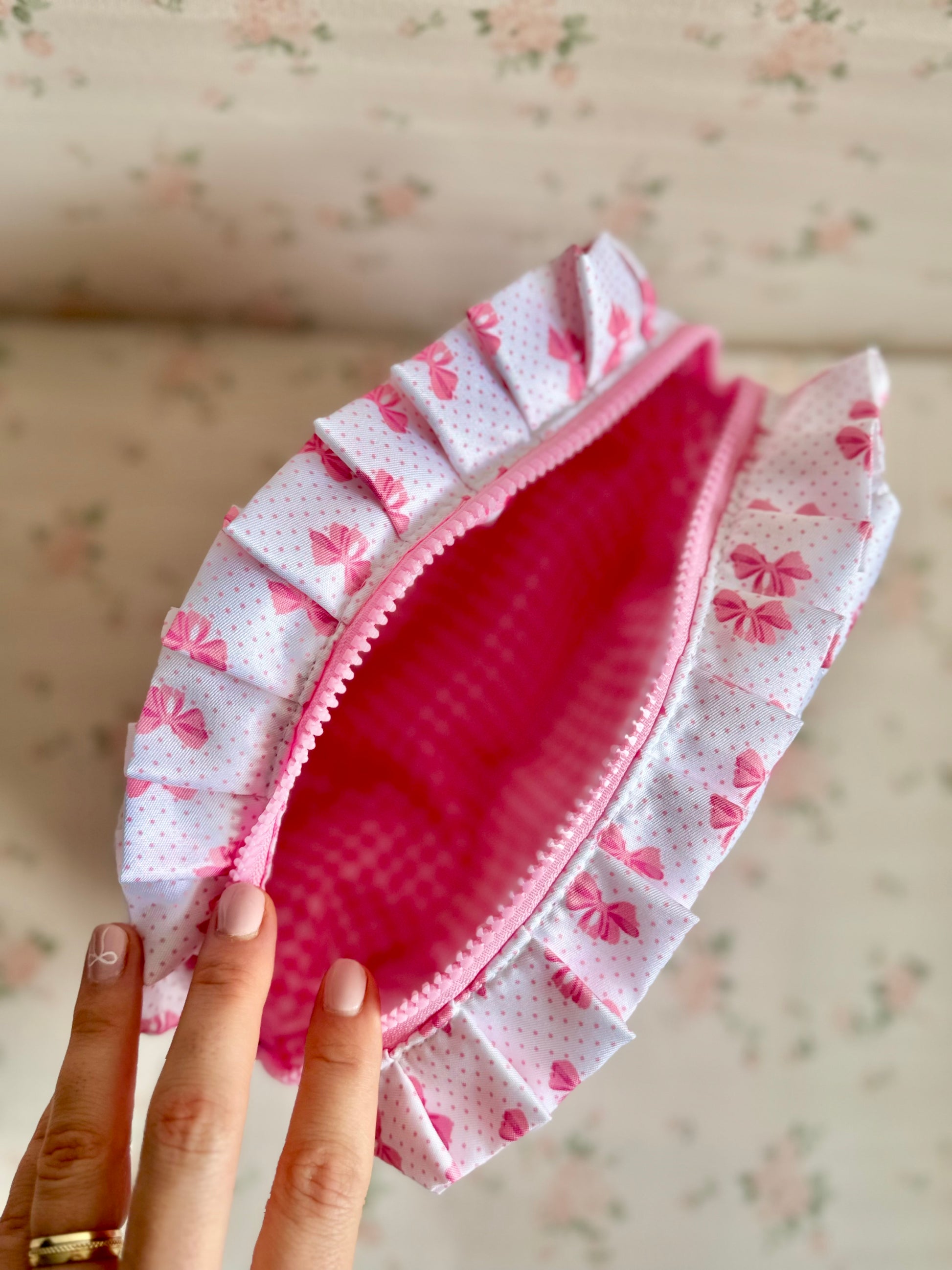 Pink and white fabric pouch with floral pattern held by a hand against a floral background