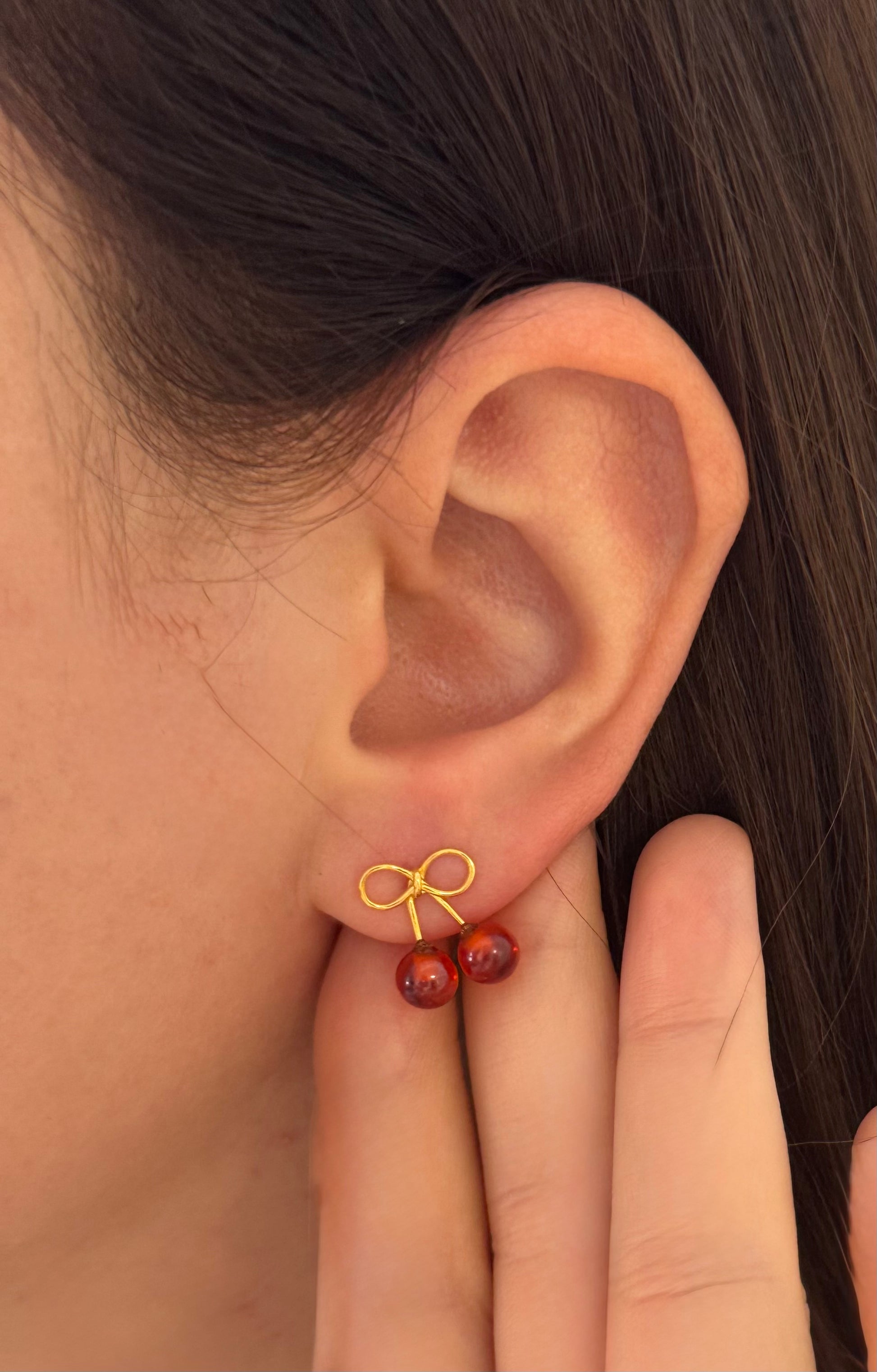Close-up of an ear wearing a gold bow earring with red beads.