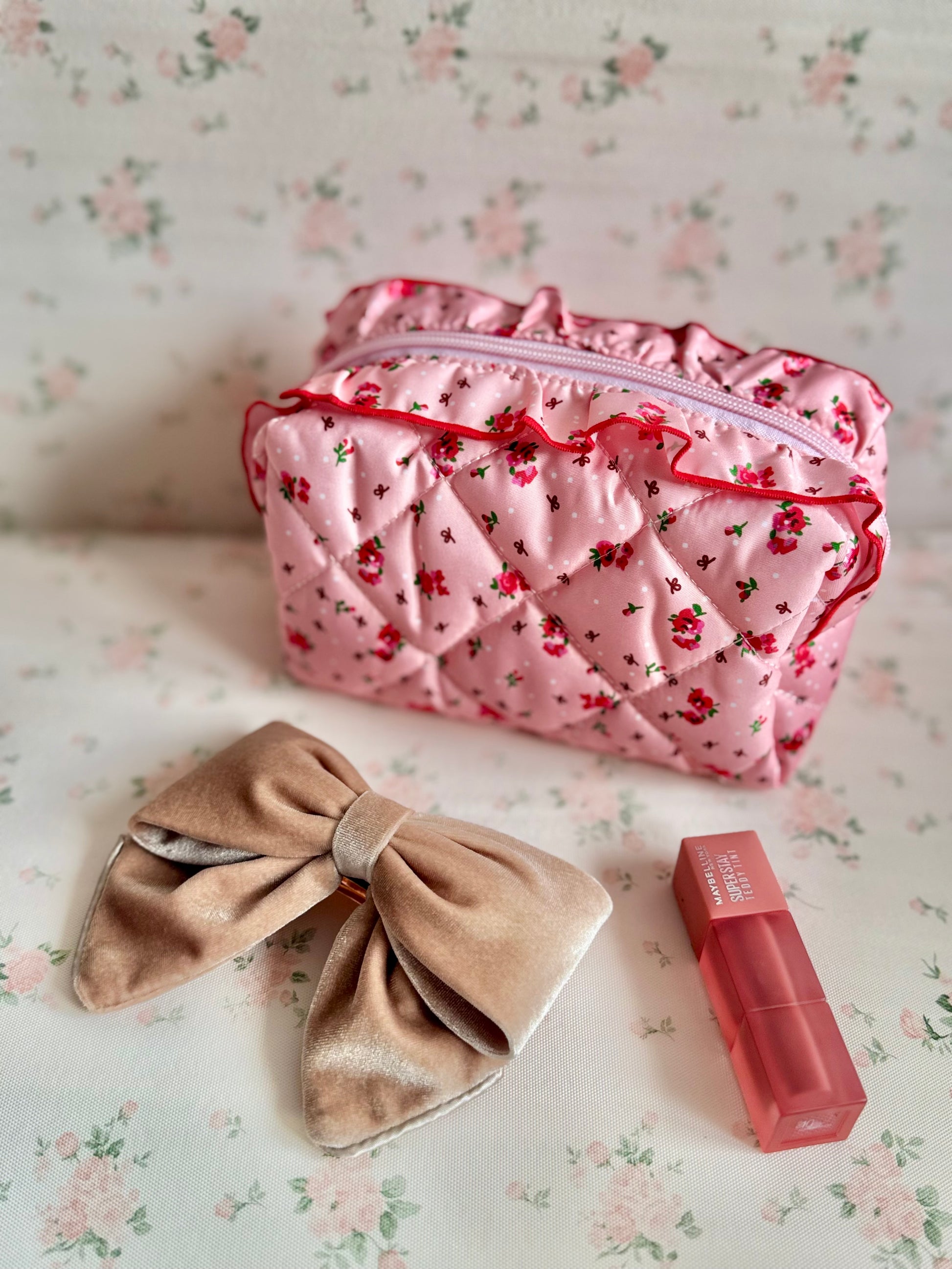 Pink floral makeup bag with a beige bow and red lipstick on a floral background