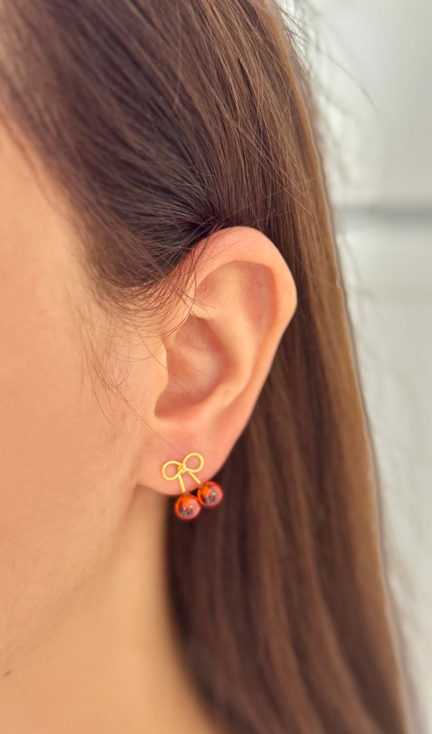 Close-up of an ear wearing a gold bow-shaped earring with red beads.
