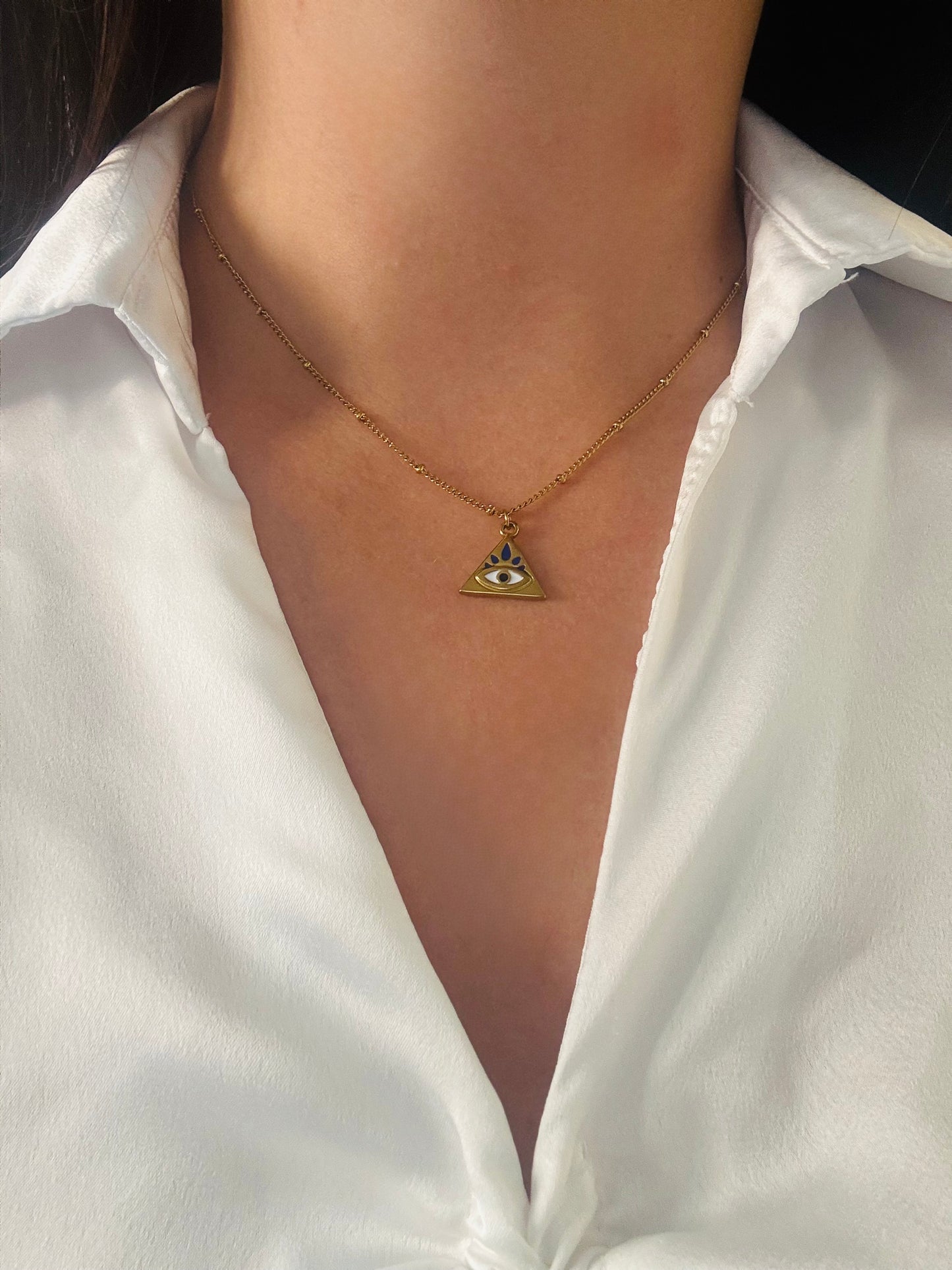 Gold necklace with a triangle pendant worn by a person in a white shirt.