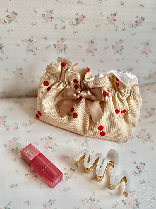 Beige pouch with red polka dots, pink lipstick, and gold hair clip on floral-patterned surface