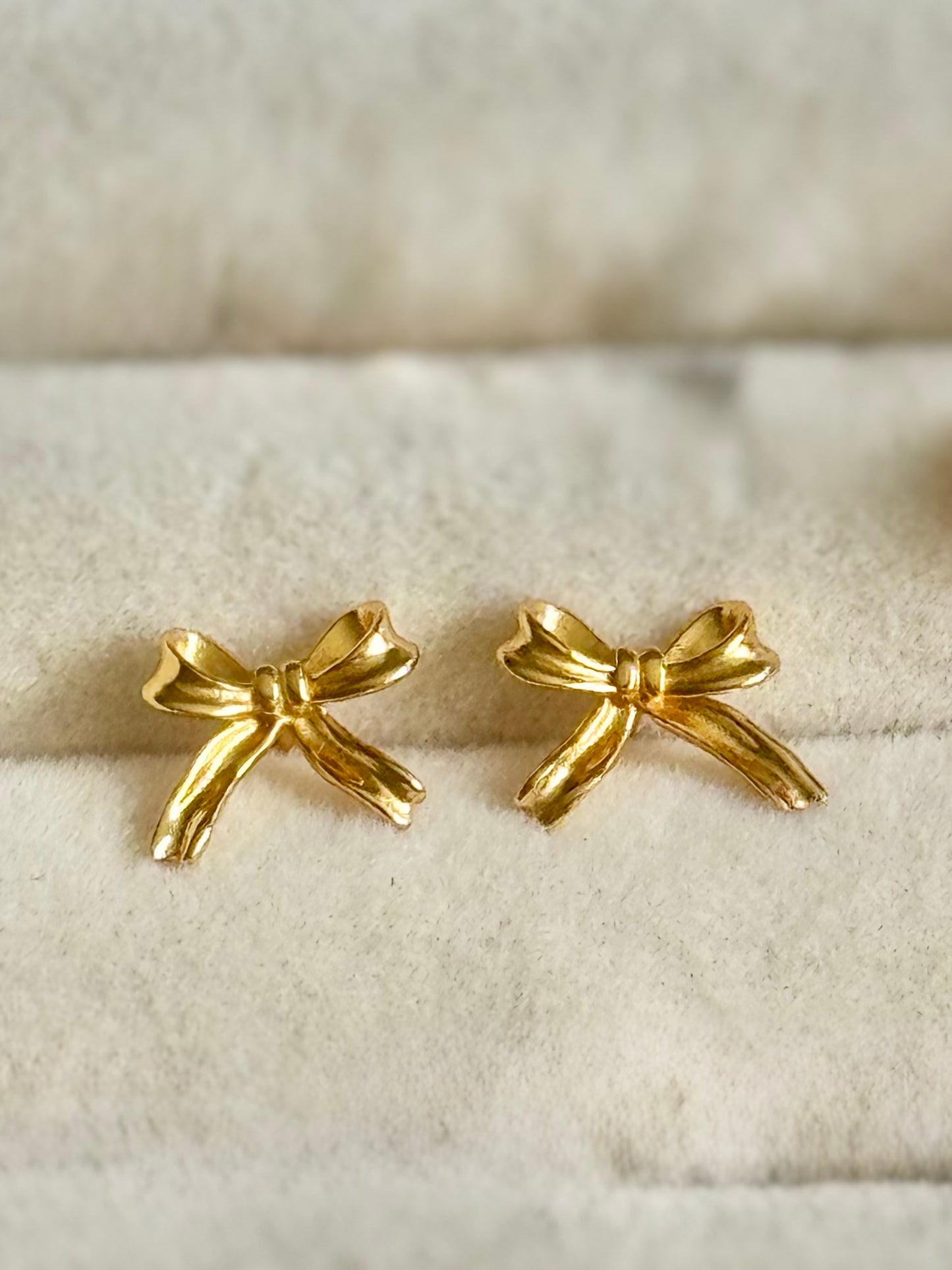 Gold bow-shaped earrings on a textured beige surface