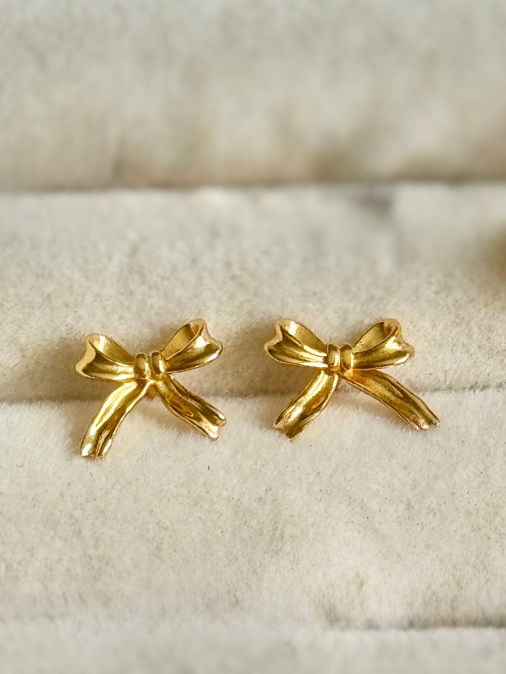 Gold bow-shaped earrings on a textured beige surface