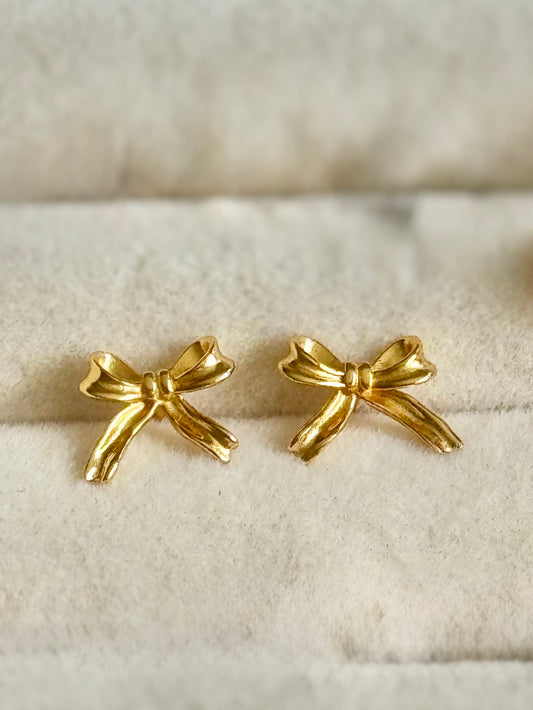 Gold bow-shaped earrings on a textured beige surface