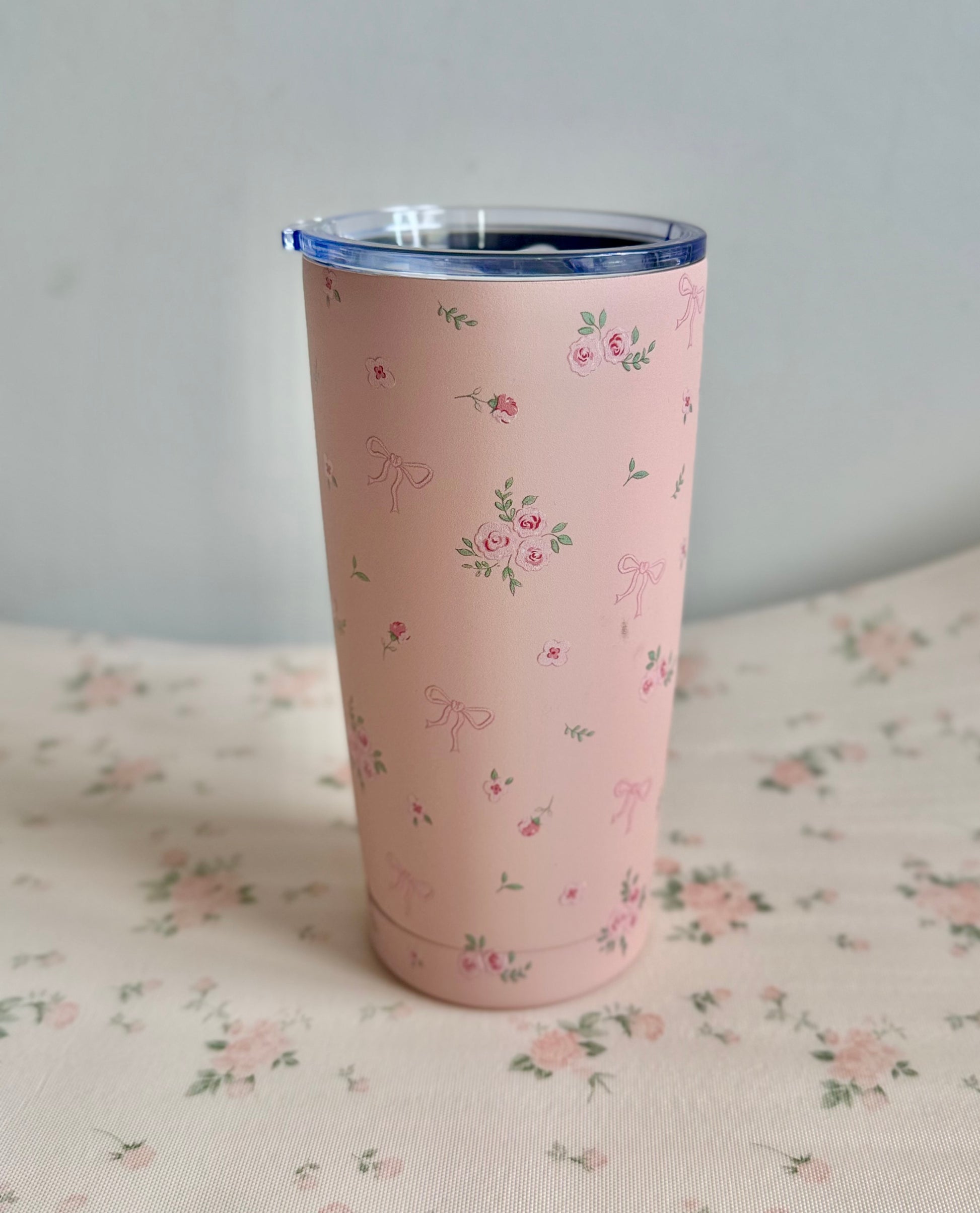 Pink tumbler with floral pattern on a floral fabric background