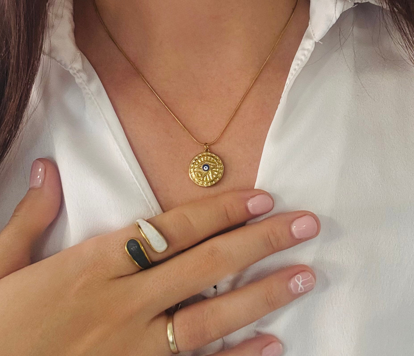 Close-up of a person wearing a gold necklace with a pendant and multiple rings on a white background