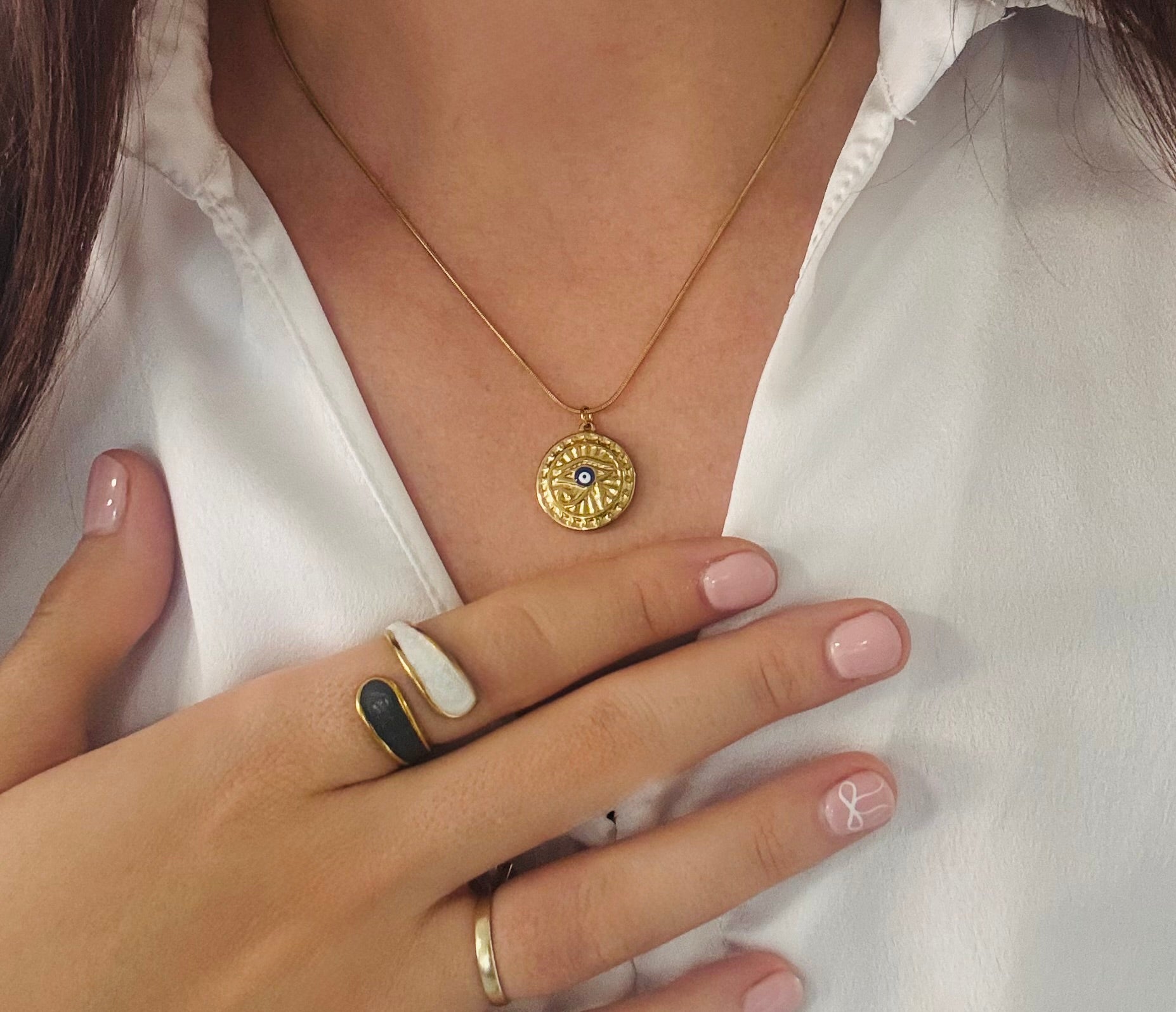 Close-up of a person wearing a gold necklace with a pendant and multiple rings on a white background