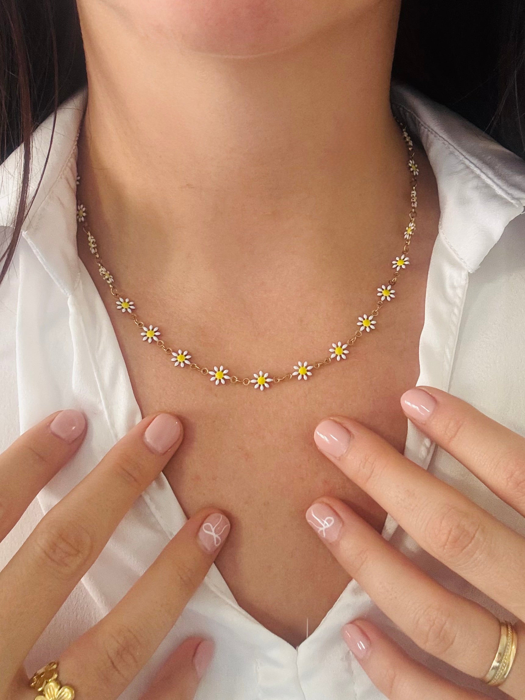 Necklace with small flowers worn by a person, close-up of the necklace and hands.