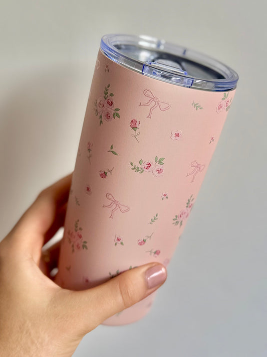 Pink tumbler with floral pattern held by a hand against a gray background