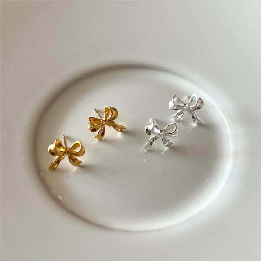 Gold and silver bow-shaped earrings on a white plate