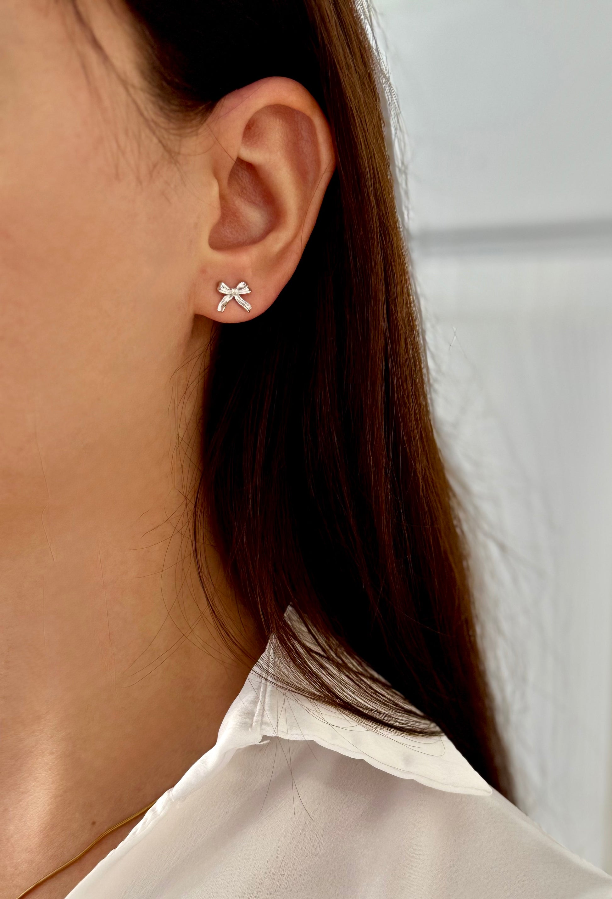 Close-up of an ear wearing a bow-shaped earring with a plain background