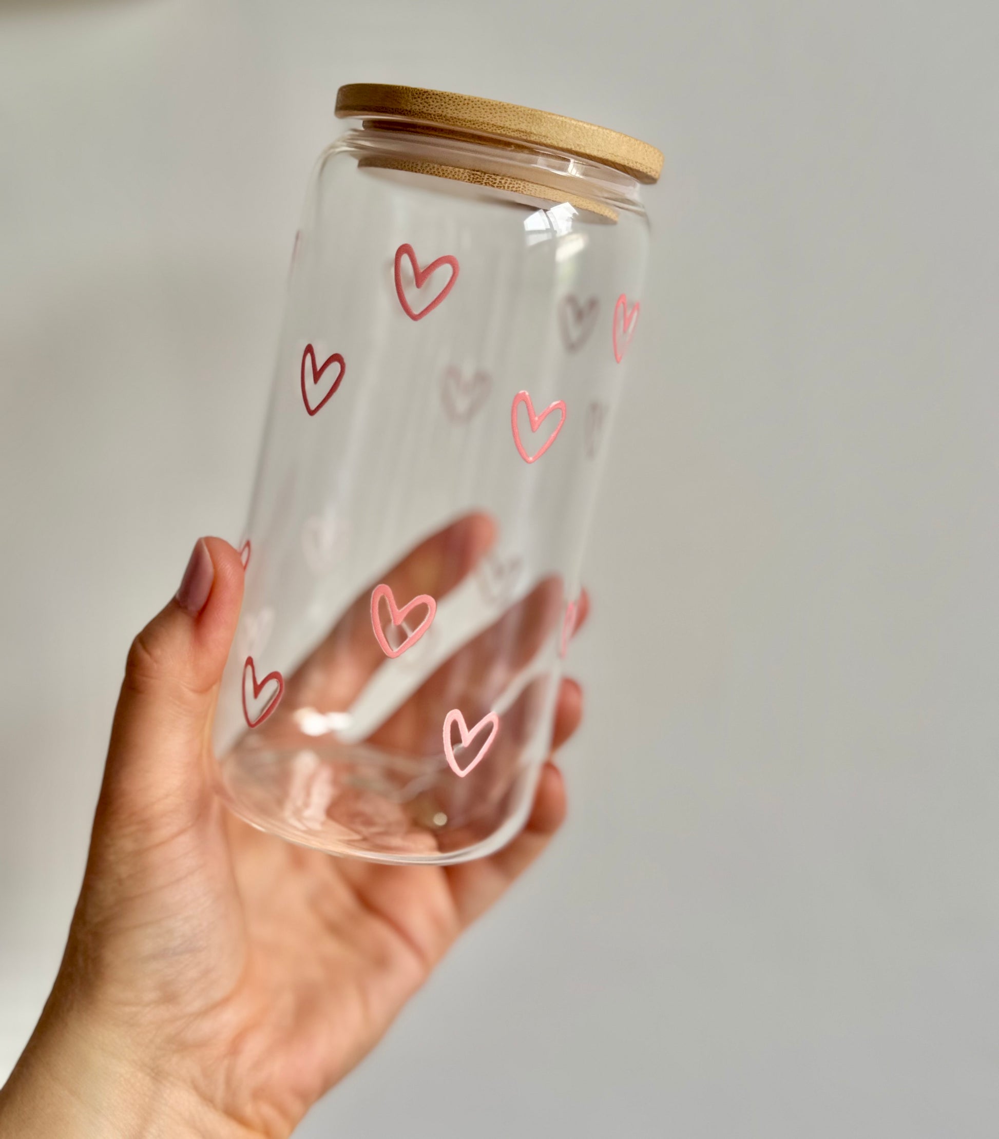Clear glass jar with pink heart designs and a wooden lid held by a hand against a plain background