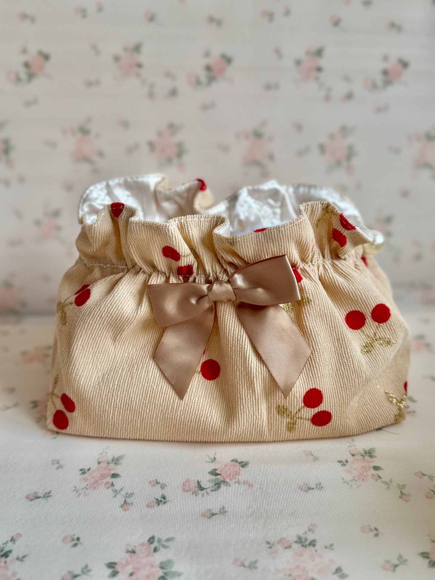 Beige fabric bag with red cherry patterns and a satin ribbon on a floral background