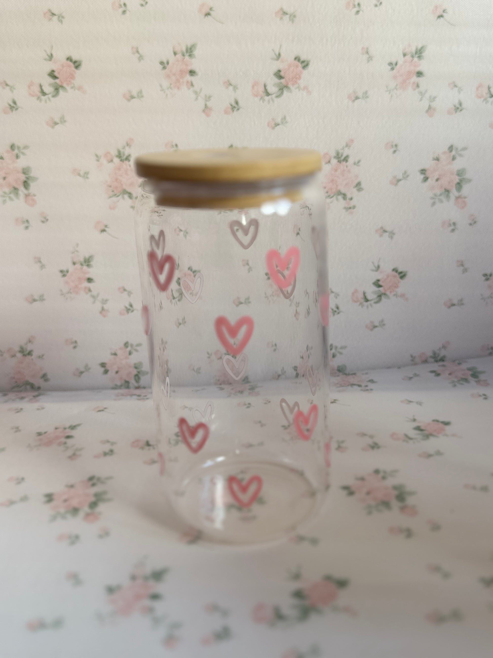 Clear glass jar with pink heart designs on a floral background