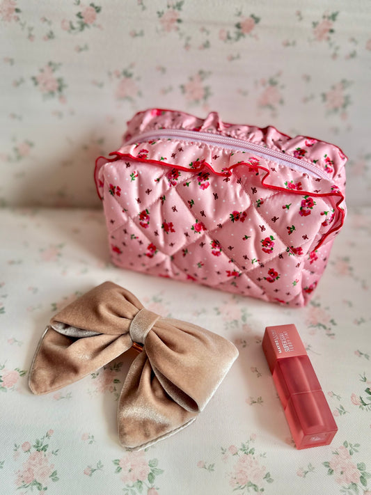 Pink floral makeup bag with a beige bow and red lipstick on a floral background