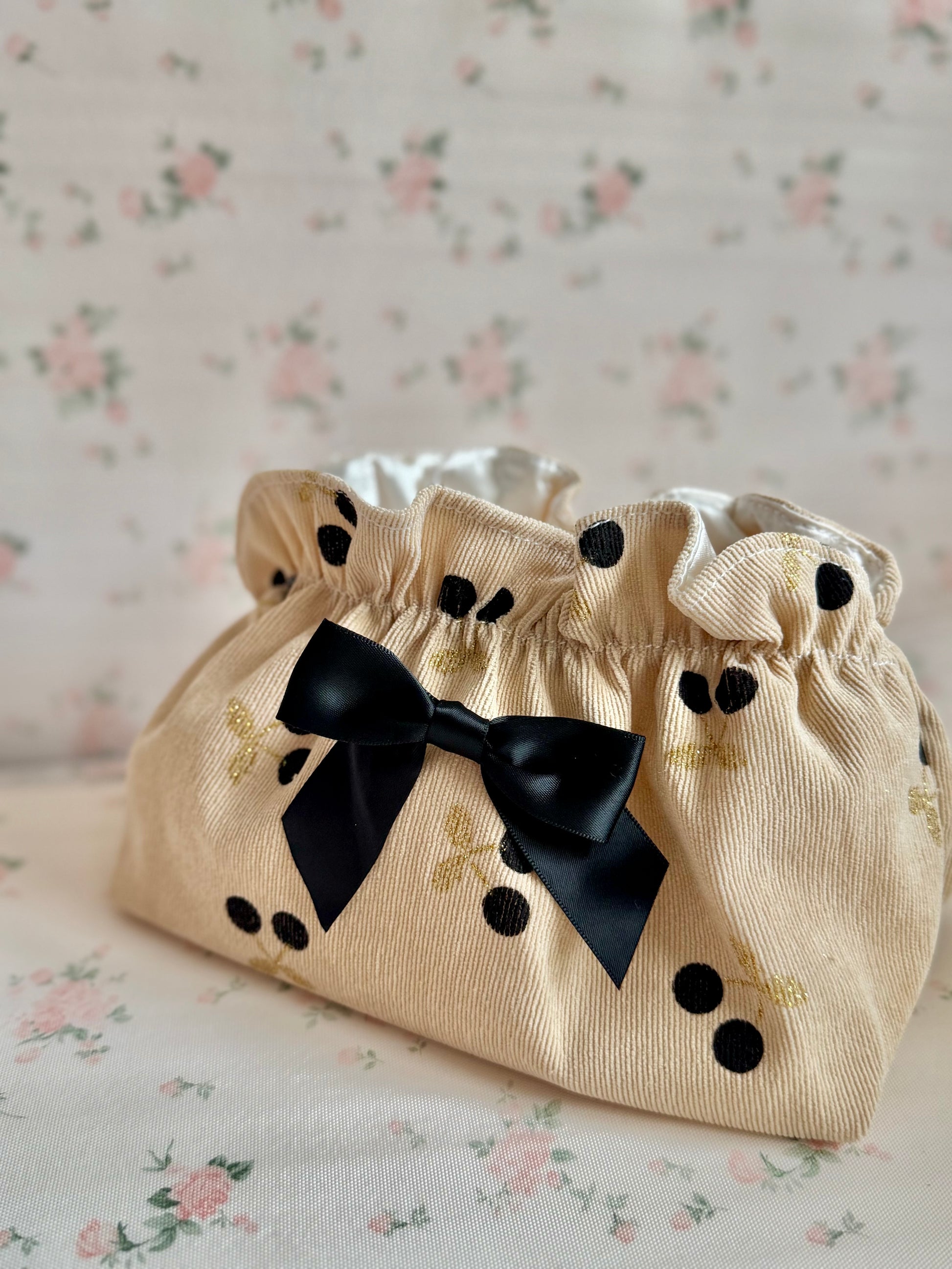 Beige fabric pouch with black bow and polka dots on a floral background