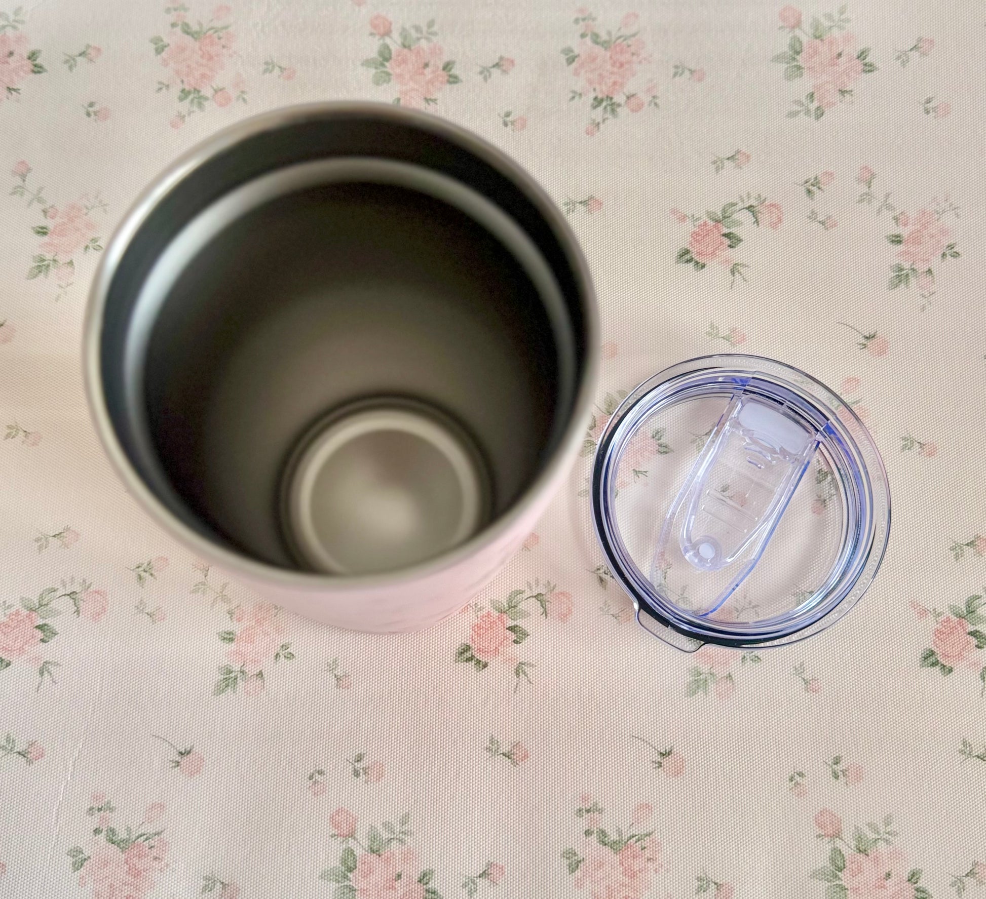 Silver tumbler with a clear lid on a floral-patterned surface